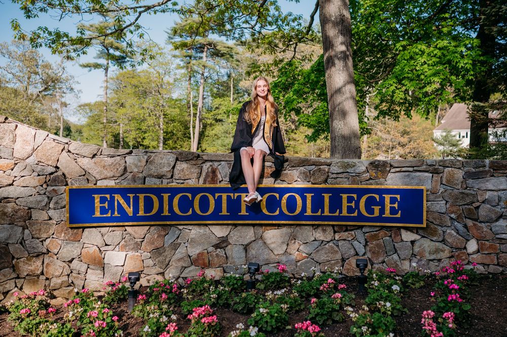 Entrance sign for Endicott College with stone wall and pink flowers blooming in a landscaped garden.