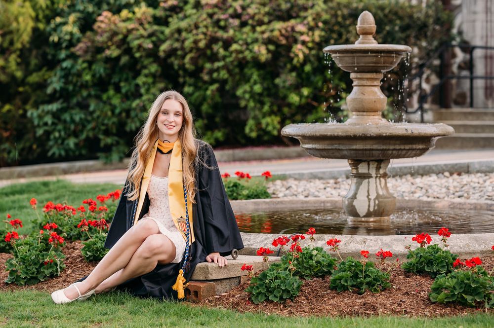 Elegant photo session in garden setting with stone fountain and blooming red flowers in background.