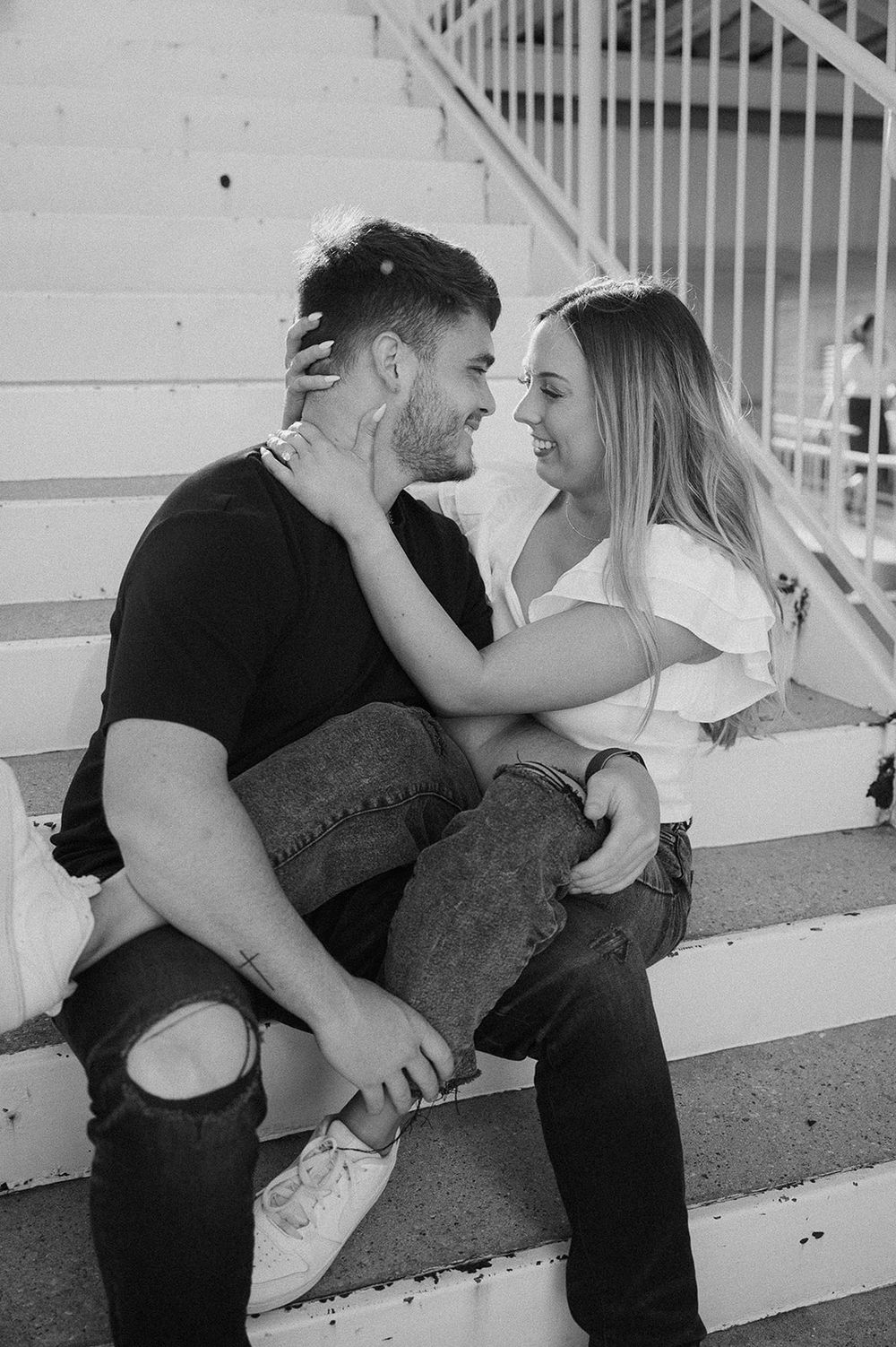 Black and white photo of a romantic couple sitting on outdoor steps sharing an intimate moment together.