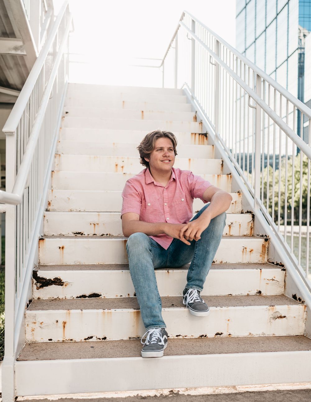 Someone wearing a pink polo shirt and jeans sits casually on white painted concrete stairs outdoors.