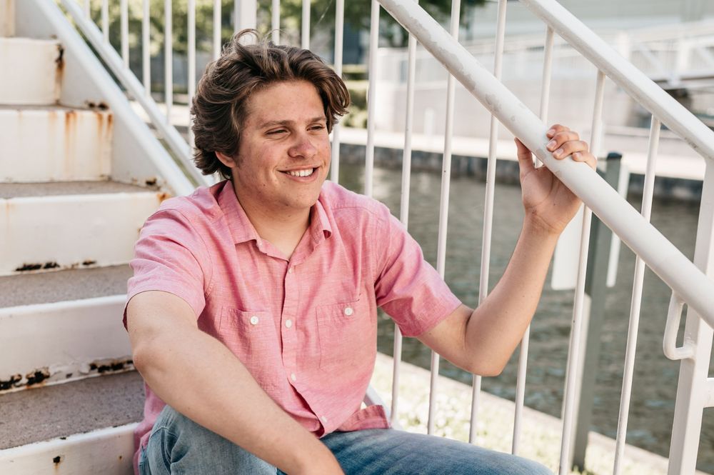 Person in casual pink shirt sits on outdoor stairs while holding railing and smiling.
