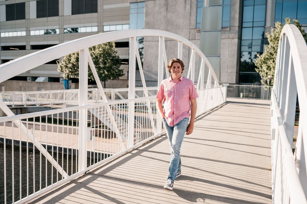 Someone wearing a pink shirt and blue jeans walks across a modern white pedestrian bridge on a sunny day.