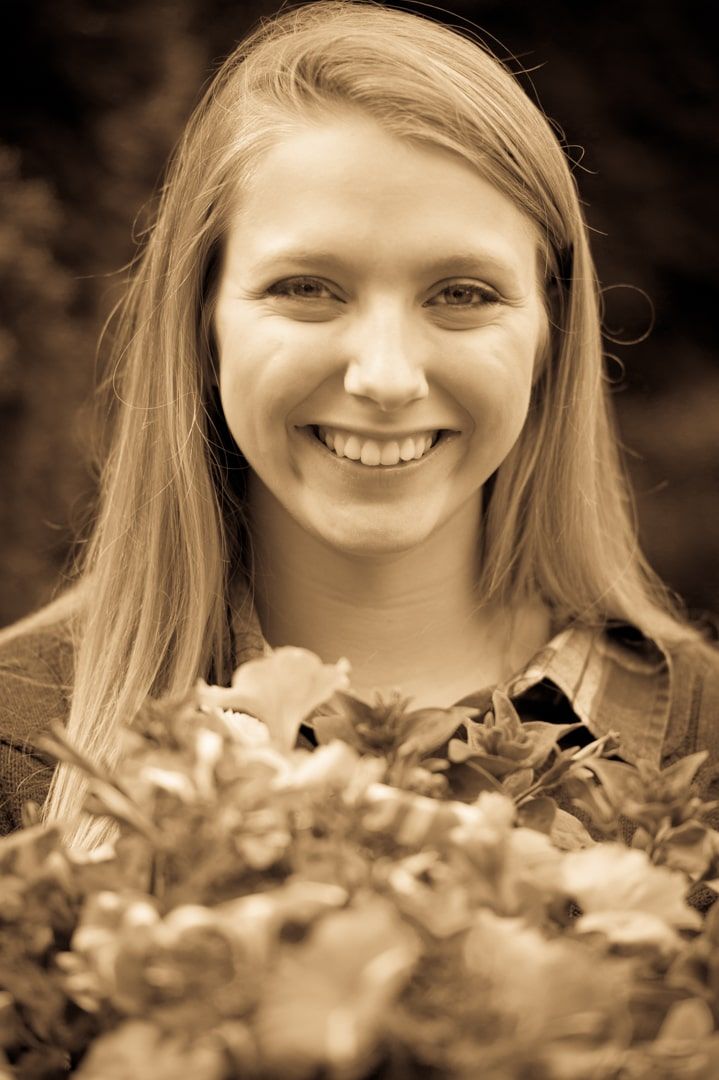 Sepia-toned female high school senior smiling, holding bouquet