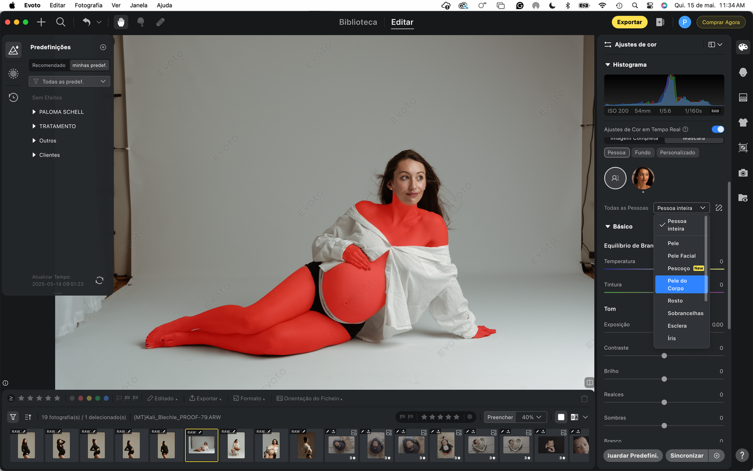 A maternity photo shoot in a studio with a white backdrop shows an artistic pose in soft lighting.