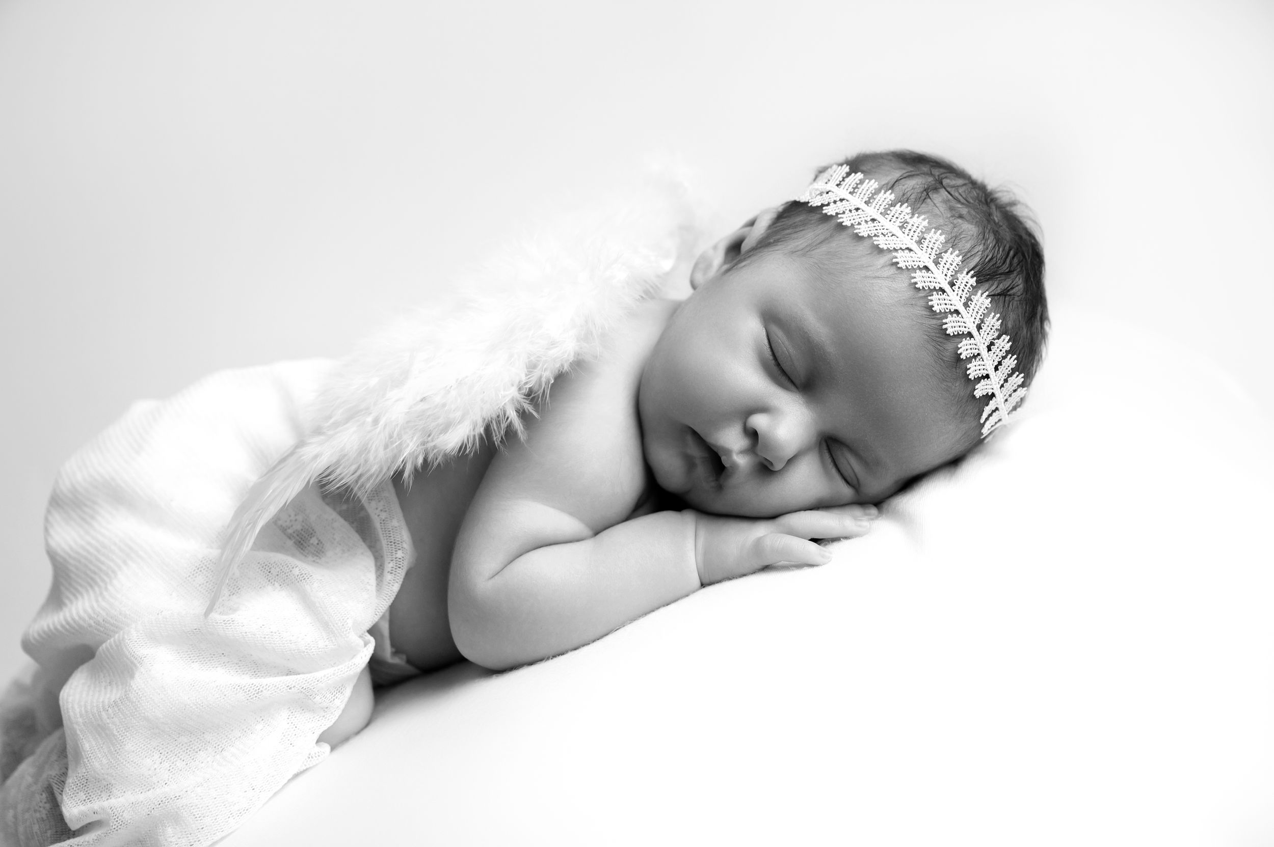 A sleeping newborn wearing a delicate white headband and tutu lays peacefully in black and white photography.
