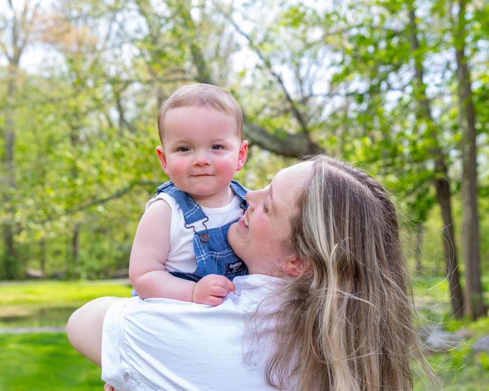 Parent and baby sharing tender moment in sunny spring garden during a Motherhood photo session in Sudbury, MA in Metrowest of Boston.