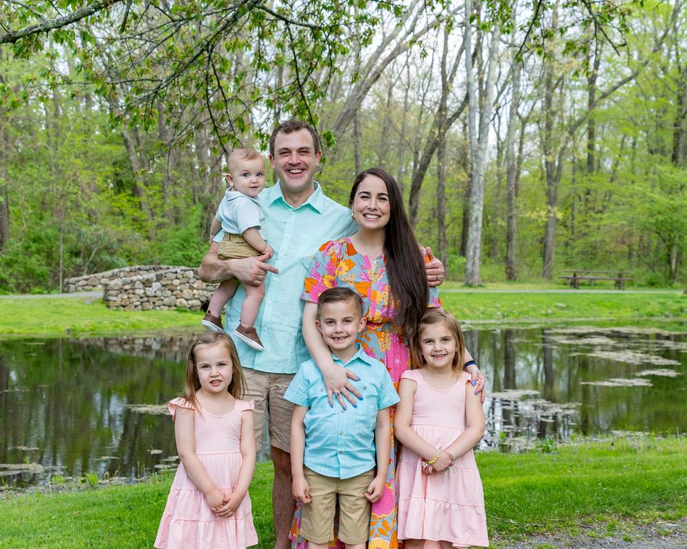 Family portrait in spring garden setting with stone wall and pond in background during a family portrait session in Sudbury, MA in Metrowest
