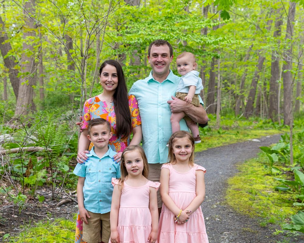 Spring family portrait with parents and children on forest path with vibrant green foliageduring a Motherhood photo session in Sudbury, MA