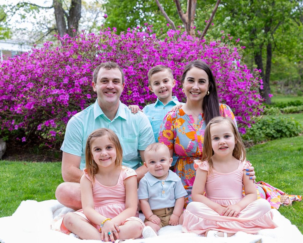 A family of six poses for a portrait in front of blooming pink azalea bushes in a garden setting in Sudbury, MA outside of Boston.