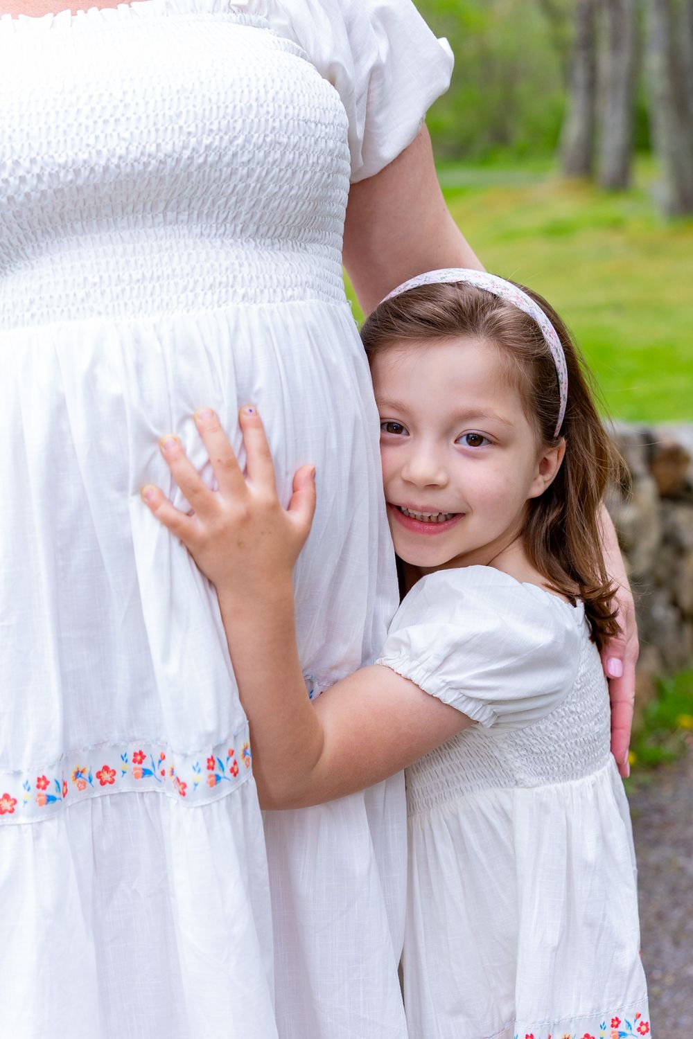 Touching moment with white dresses and floral embroidery details outdoors during a family portrait photo session in Sudbury, MA