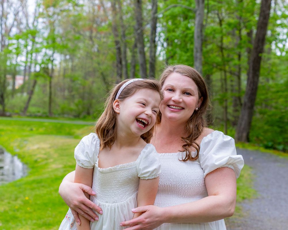 Joyful outdoor portrait with matching white dresses against green forest backdrop during a family portrait photo session in Sudbury, MA