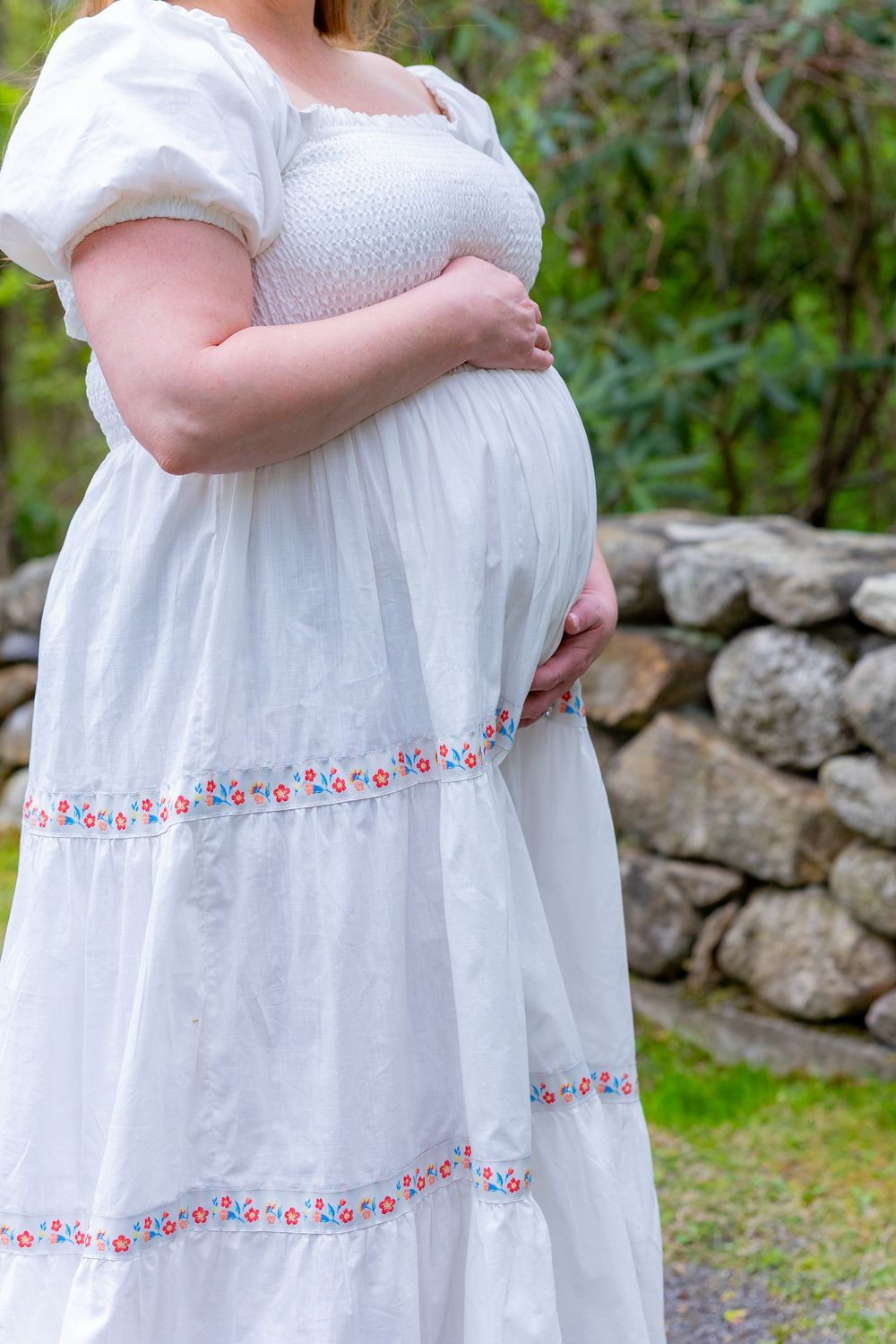 Detail shot of white maternity dress with delicate floral embroidery trim during a maternity photo session in Sudbury, MA in Metrowest