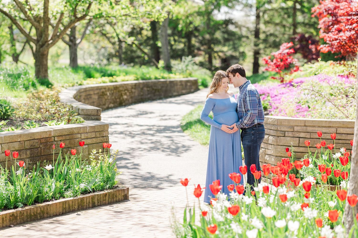 A couple stands together on a garden path surrounded by vibrant spring tulips and blooming flowers in a scenic park setting at Chicago Botan