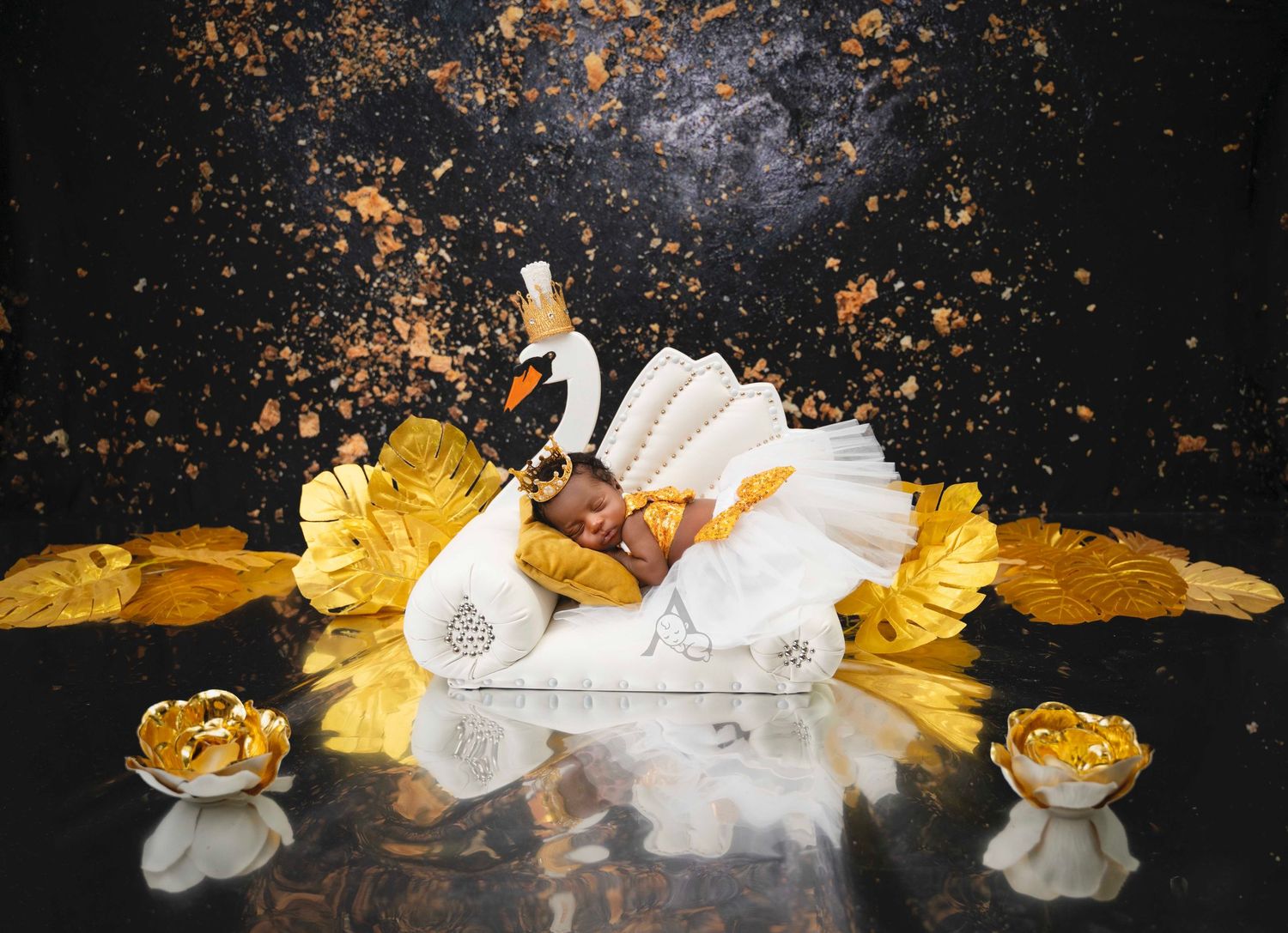 Artistic newborn photography setup with swan prop and golden accents on dark reflective surface.