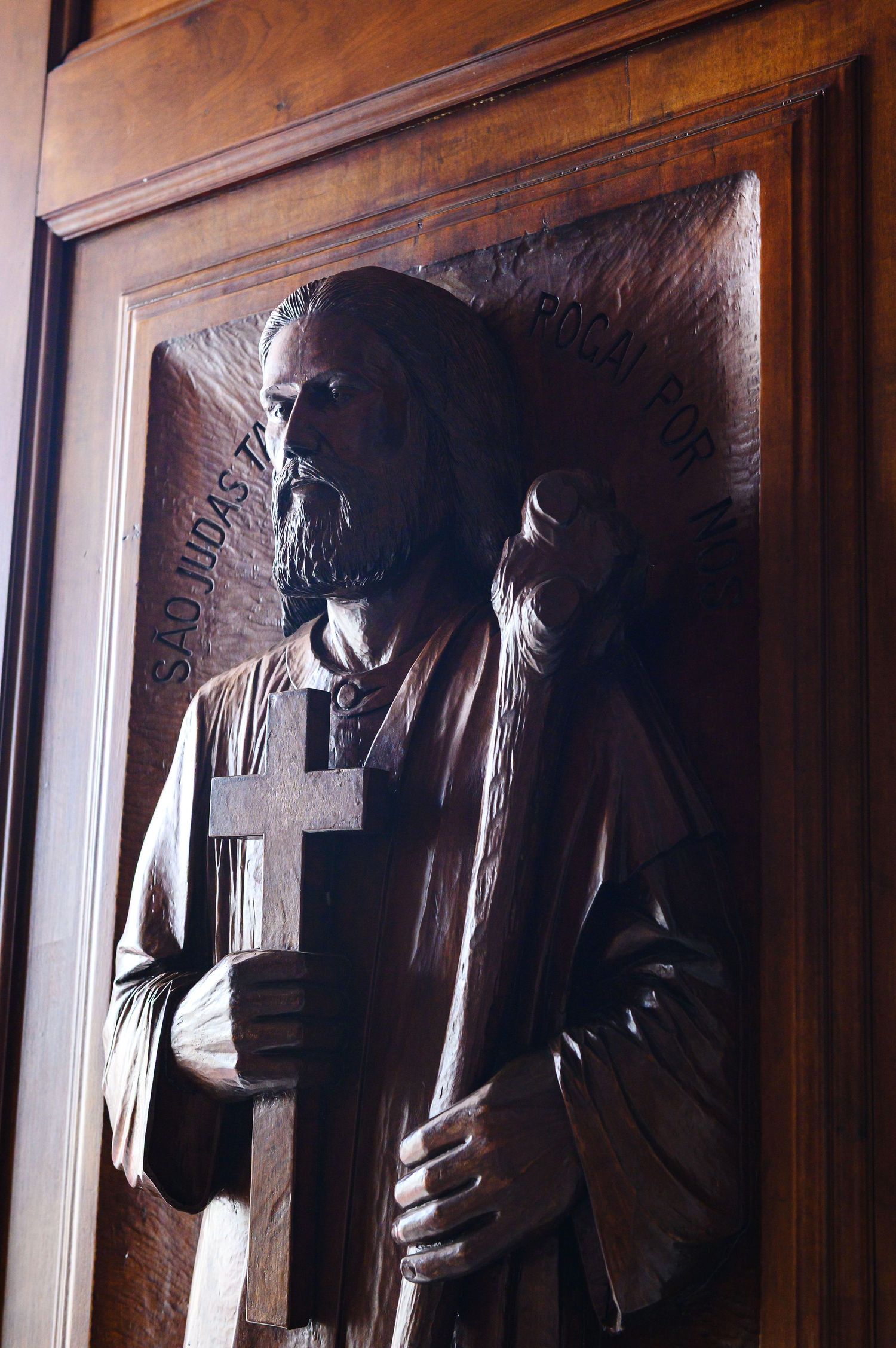 Intricate wooden carving relief of a robed figure holding a cross on a church door panel.