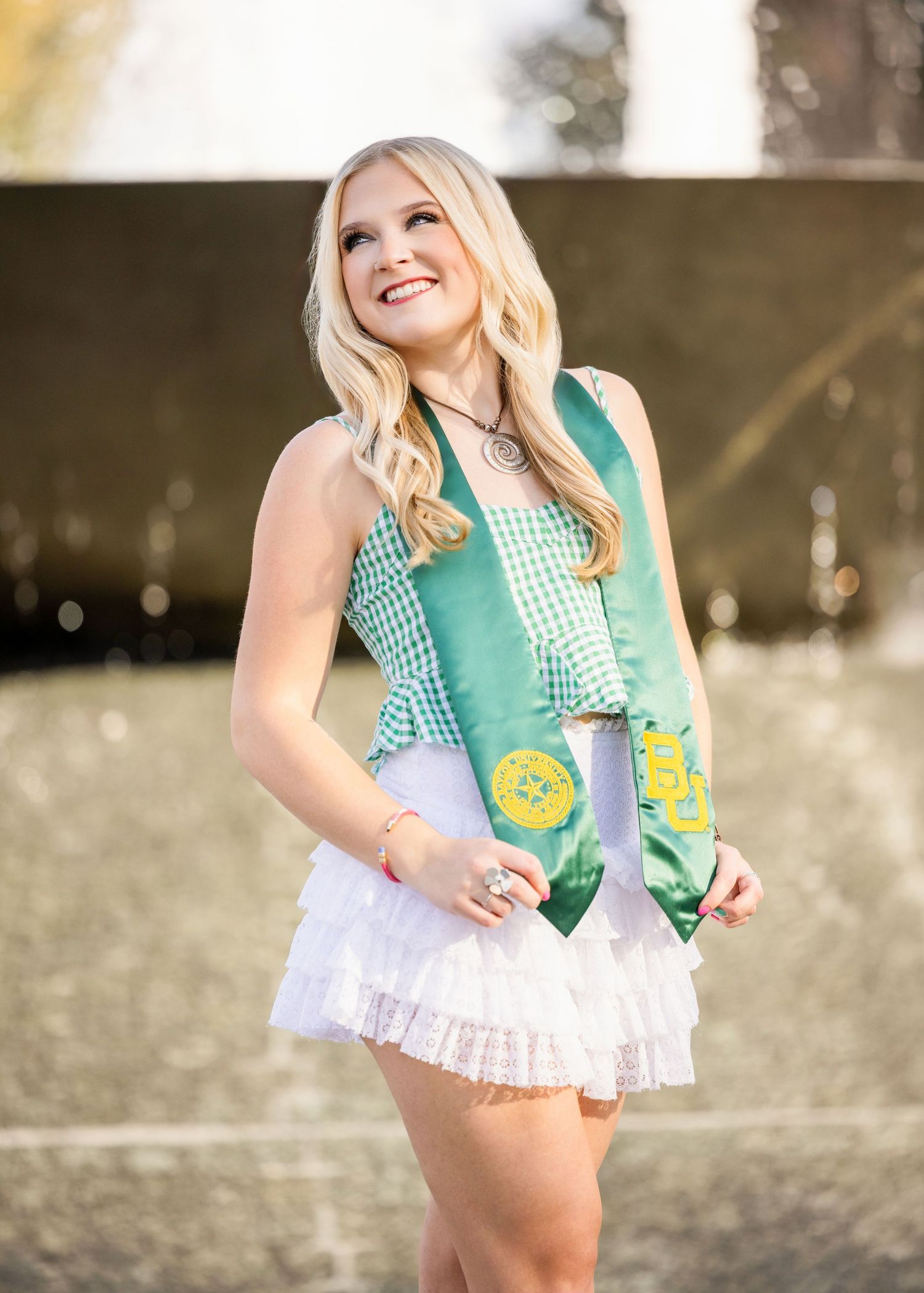 A scout in a green vest with merit badges and white ruffled skirt stands smiling outdoors in natural lighting.