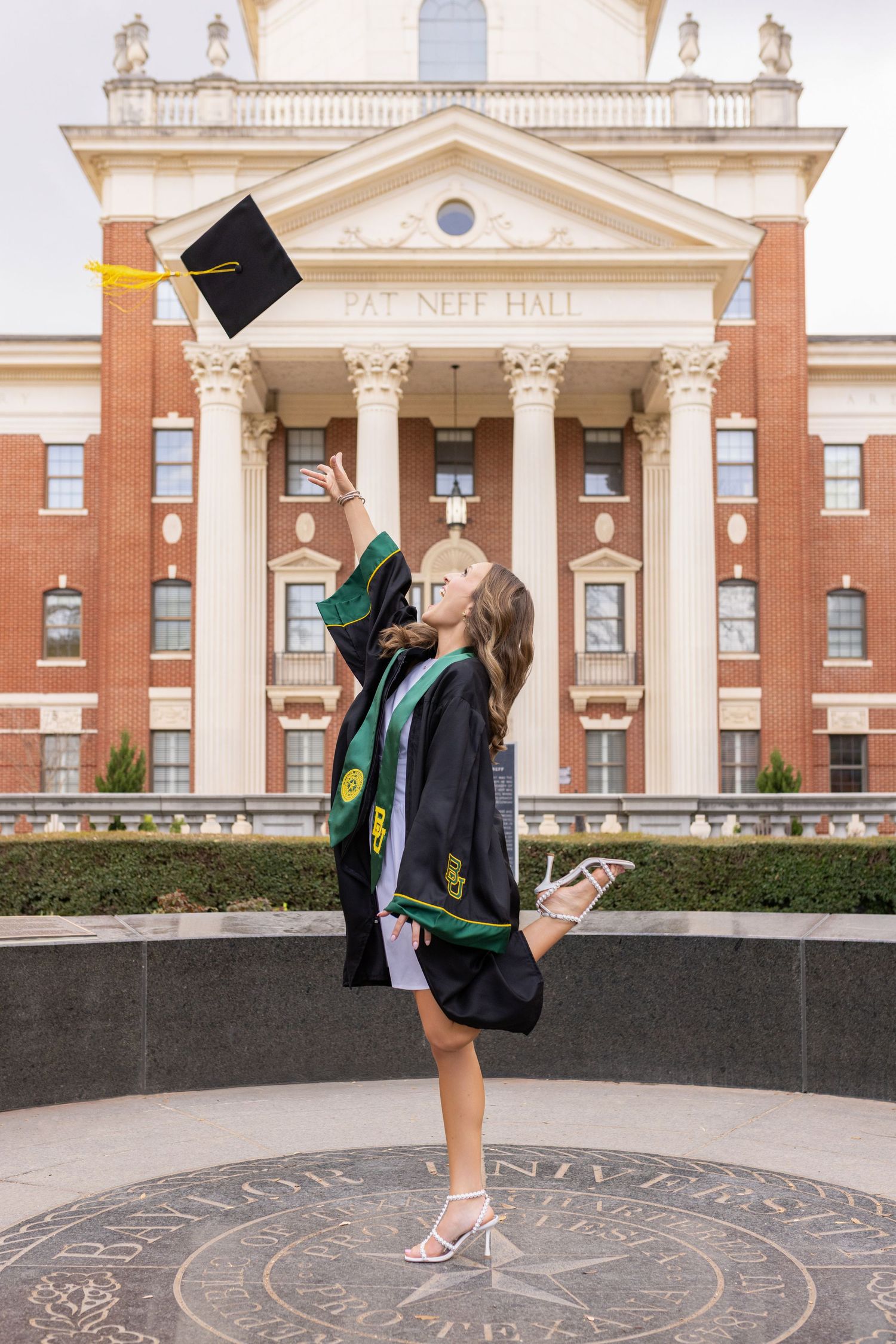 Graduate celebrates with cap toss in front of ornate university hall with classical columns and architecture.