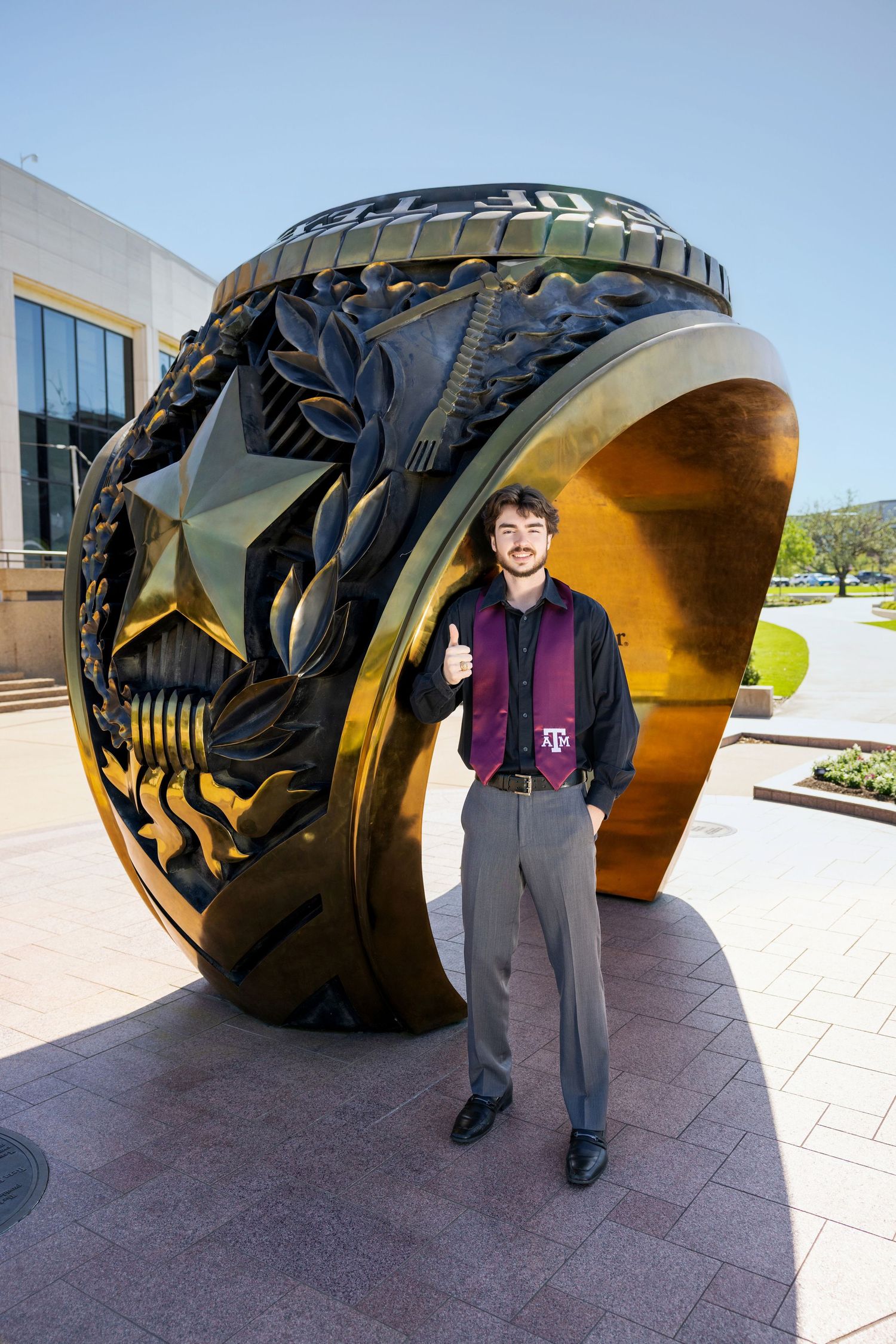 A giant Aggie ring sculpture with decorative military-inspired designs stands outside a building at Texas A&M University.
