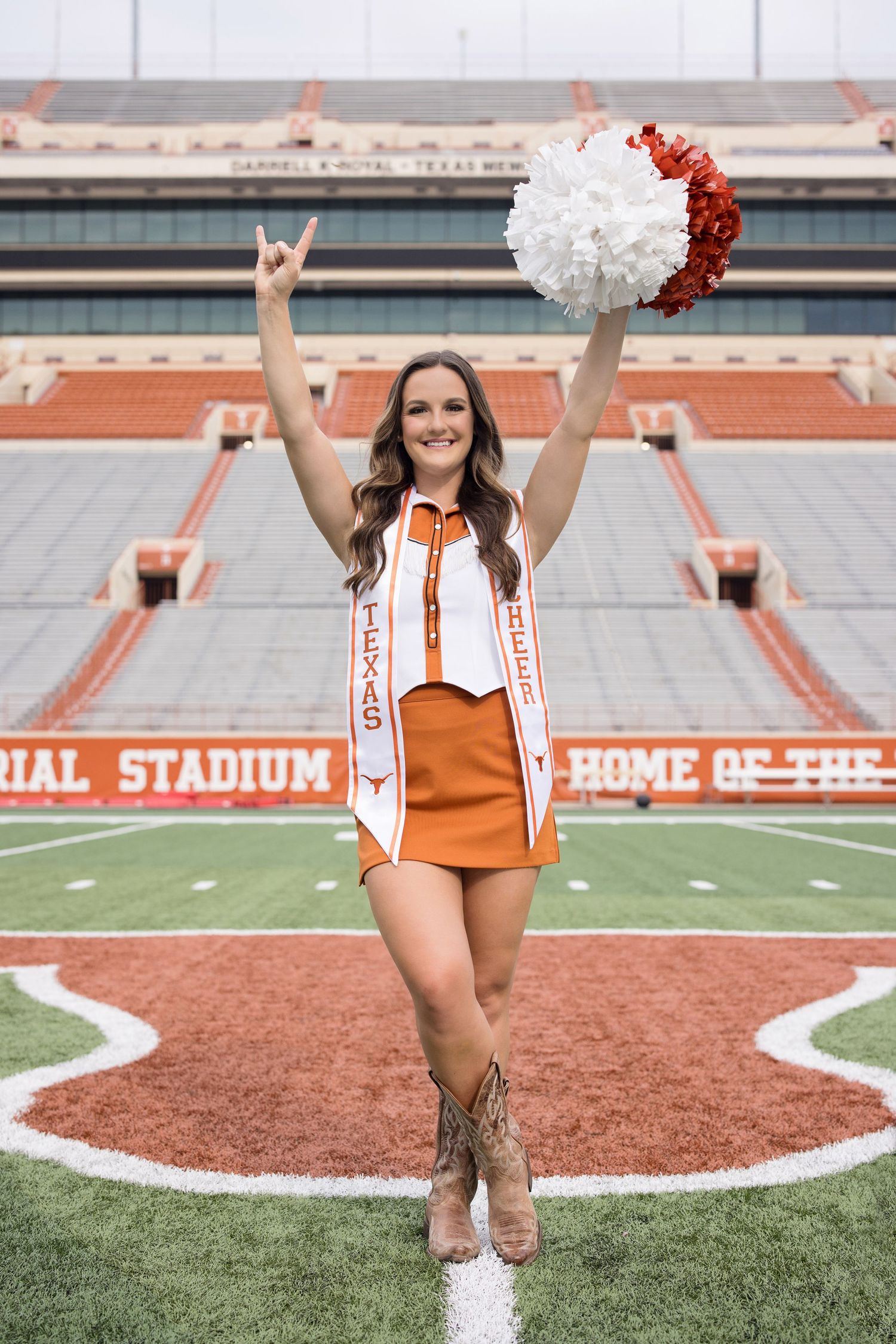 A cheerleader in an orange uniform poses with pom poms at Texas Memorial Stadium in Austin.