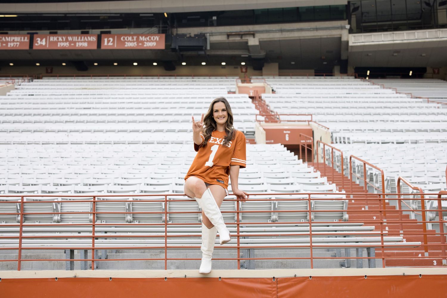 Someone in burnt orange attire posing playfully on bleacher steps at a stadium.