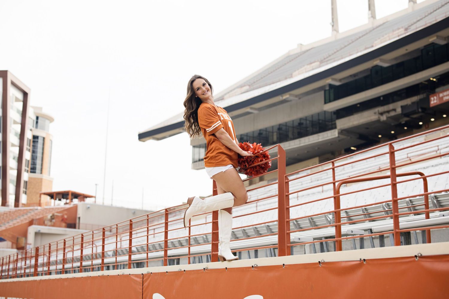 A model in an orange dress poses gracefully on orange stadium bleachers with sunlight casting a warm glow.