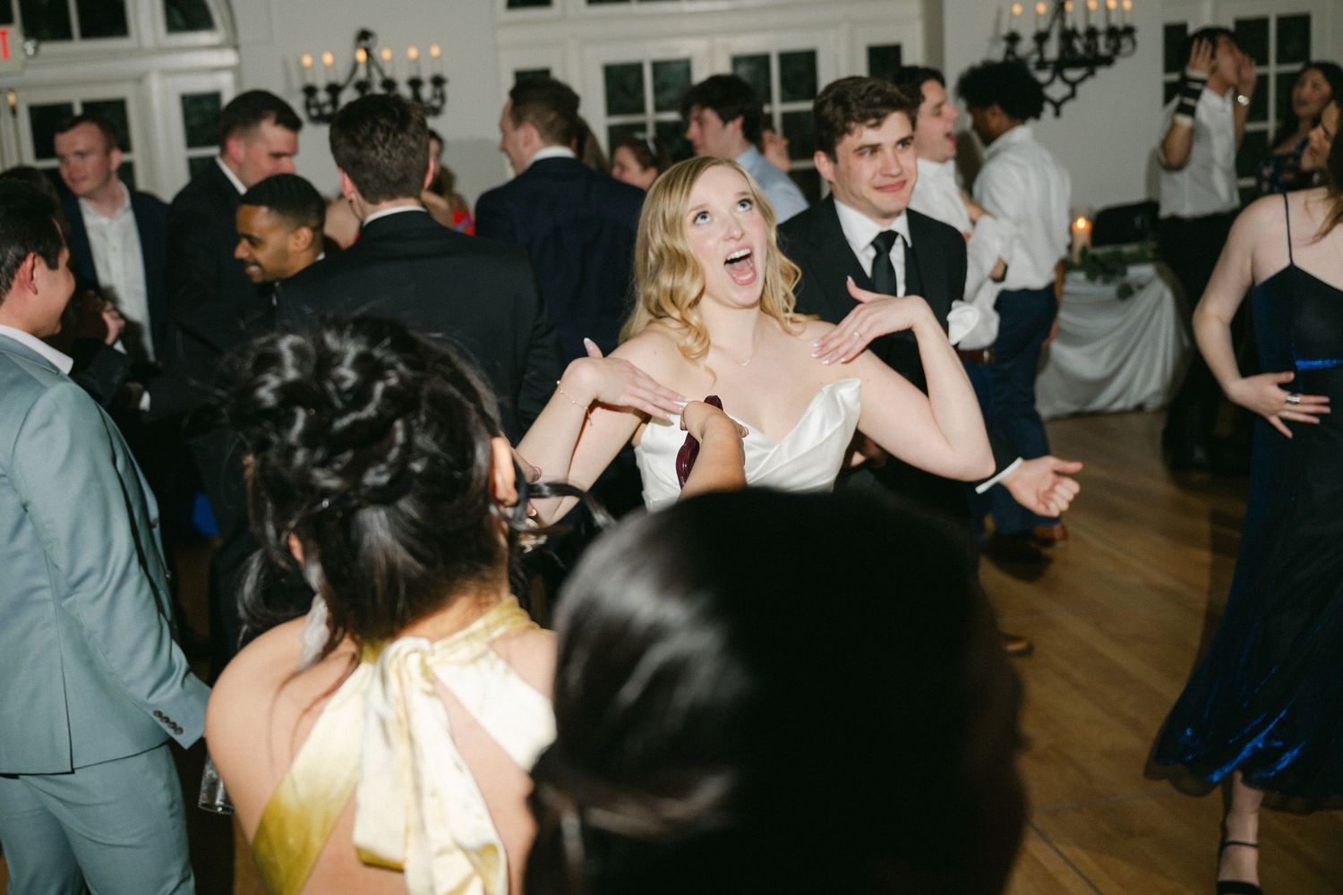 Wedding guests dance with raised hands on a dark dance floor during an energetic reception celebration.