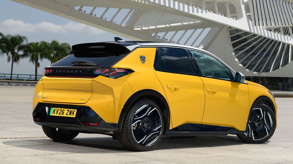 A sporty yellow Peugeot e-2008 electric SUV parked in front of modern architecture with curved white beams and palm trees.