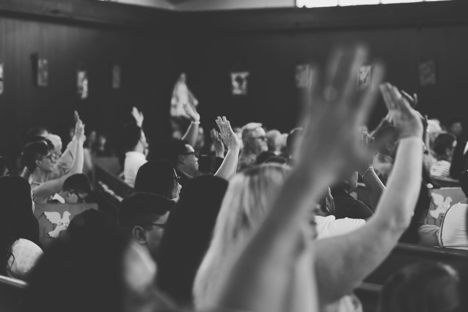 Black and white image of a congregation with raised hands in a catholic first communion mass showing energetic participation.