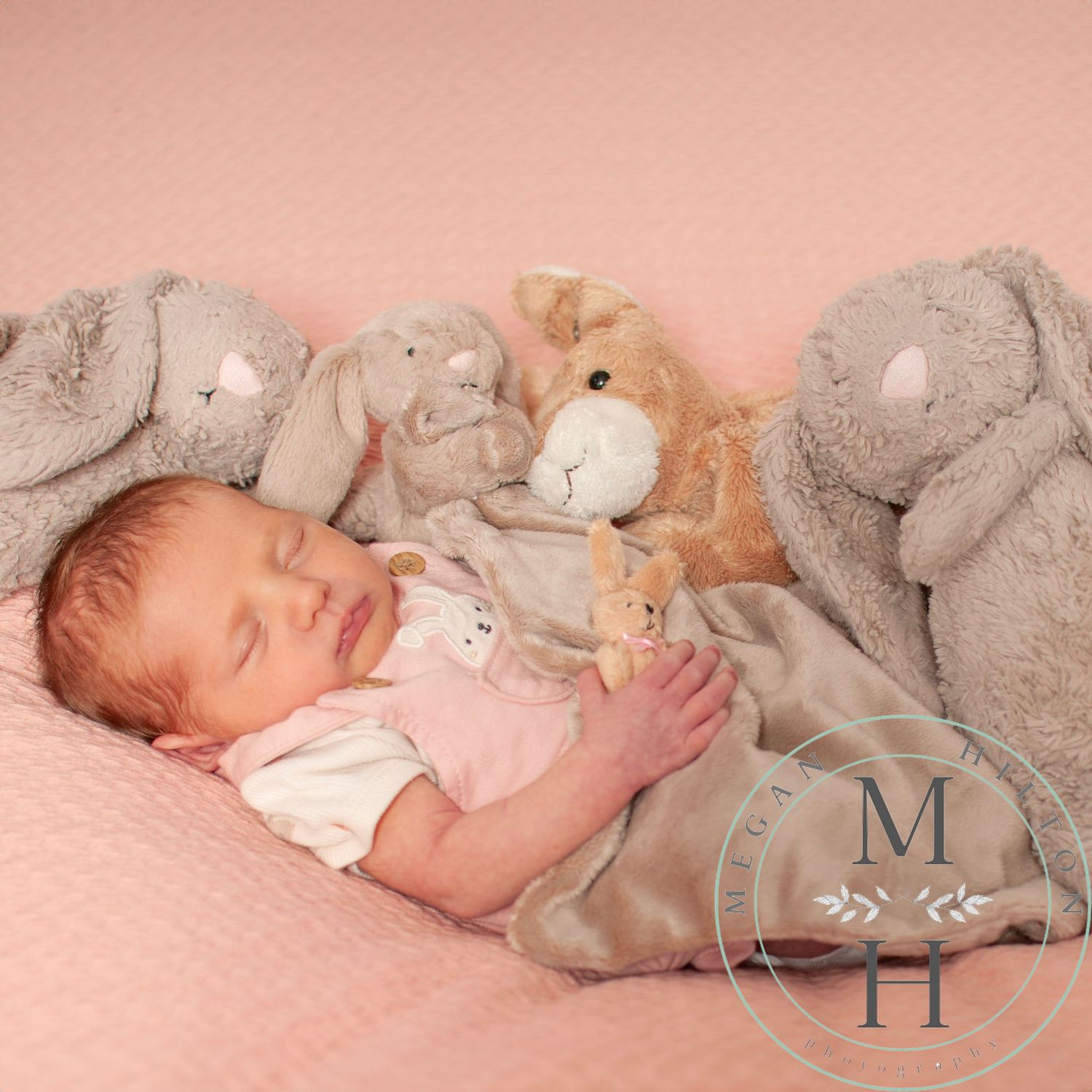 A sleeping baby rests peacefully among soft plush animal toys on a pink background.