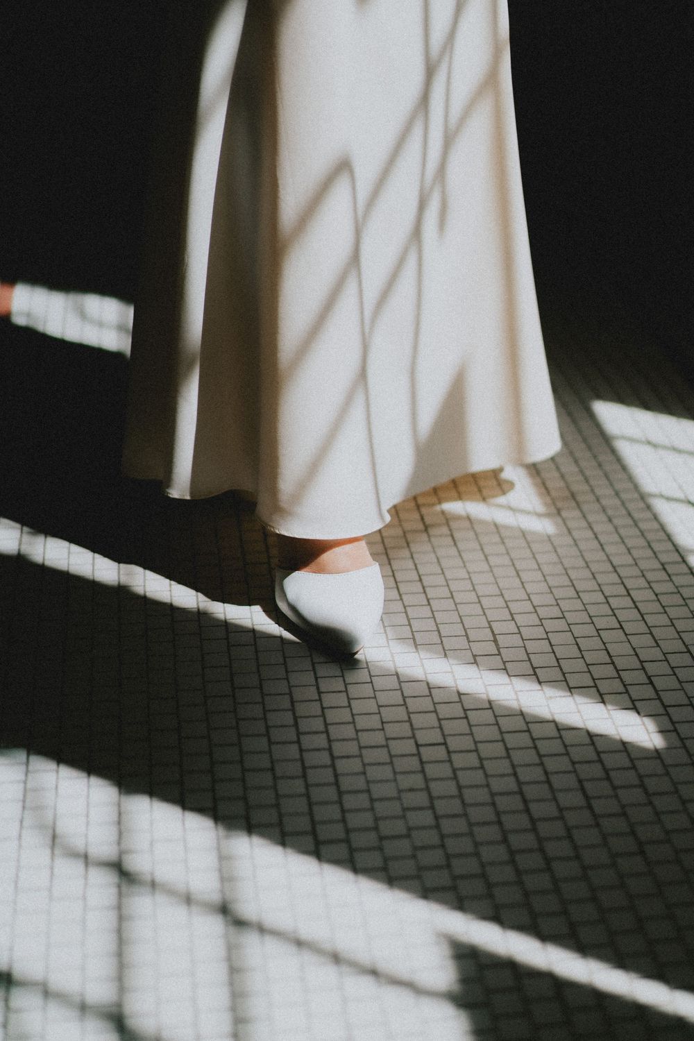 White dress and shoes casting dramatic shadows on a tiled floor in minimalist composition.