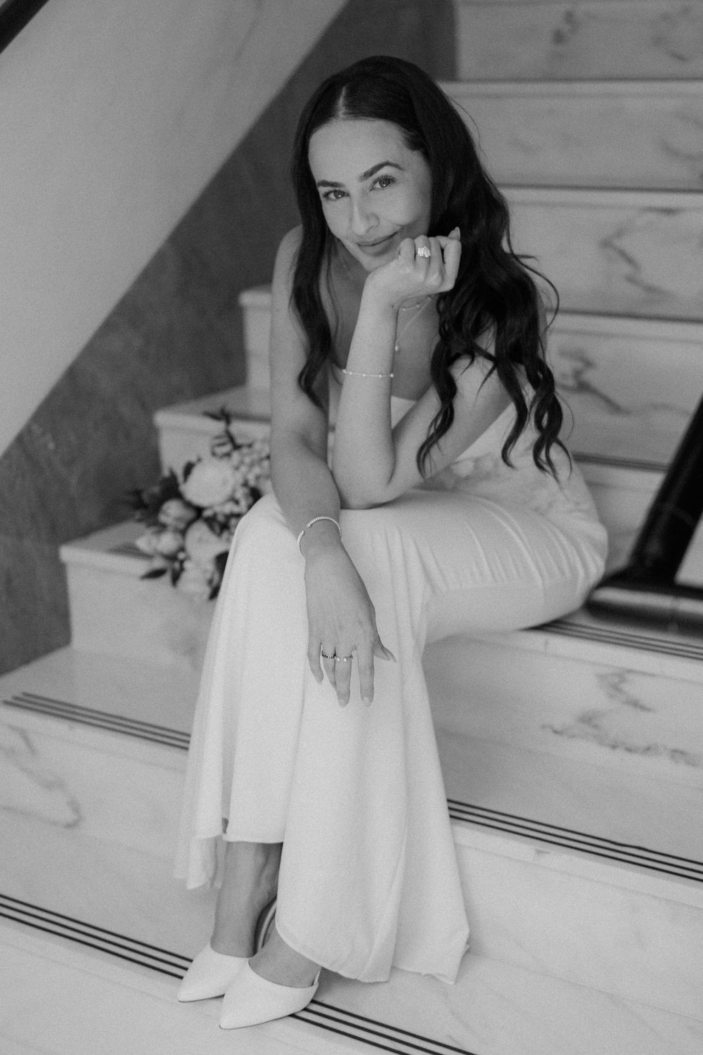 Black and white portrait photo of a woman in a white dress sitting elegantly on marble stairs.