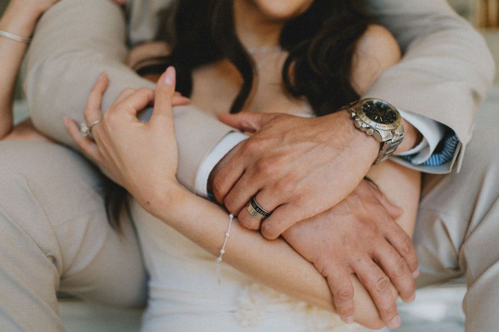 A close up detail shot showing hands with wedding rings and a luxury watch against formal wedding attire.
