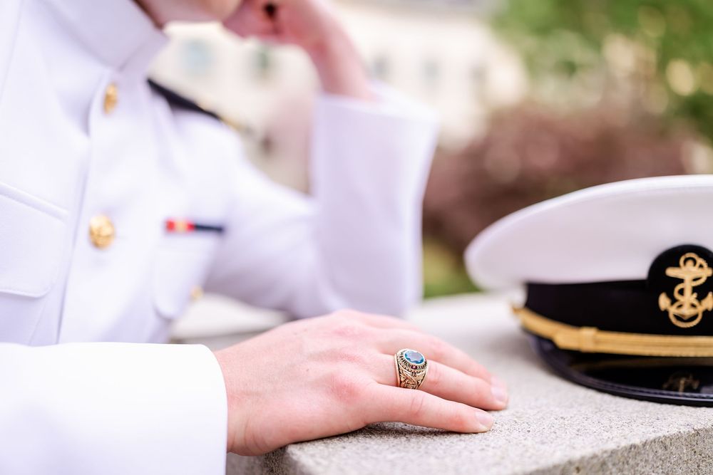 Close-up of naval officer's uniform with class ring and cap visible.