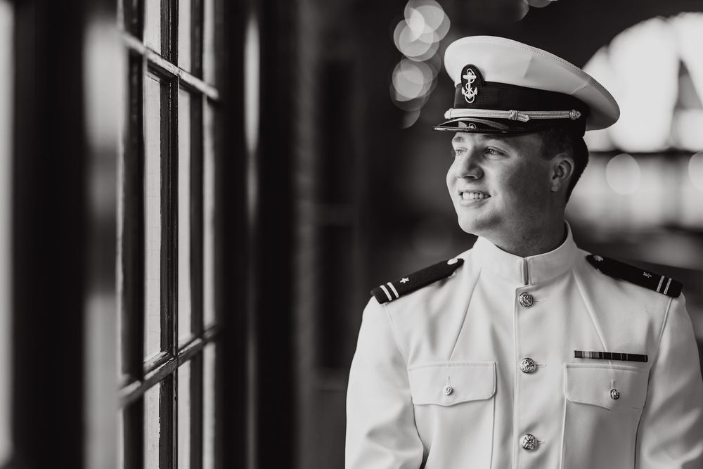 Naval officer in white dress uniform looking pensively through window in black and white portrait.