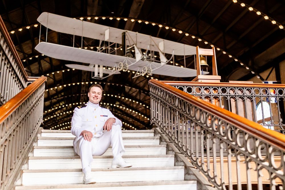 Person in white attire sitting on an ornate staircase with a vintage airplane model displayed overhead.