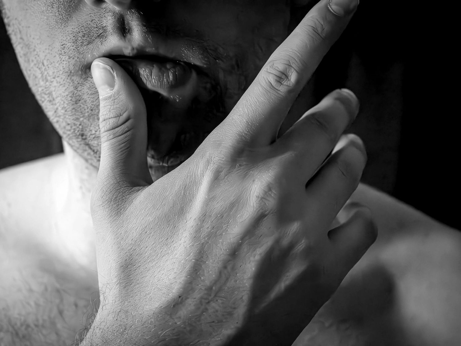 Close-up black and white photo showing a hand raised to lips in a suggestive manner.