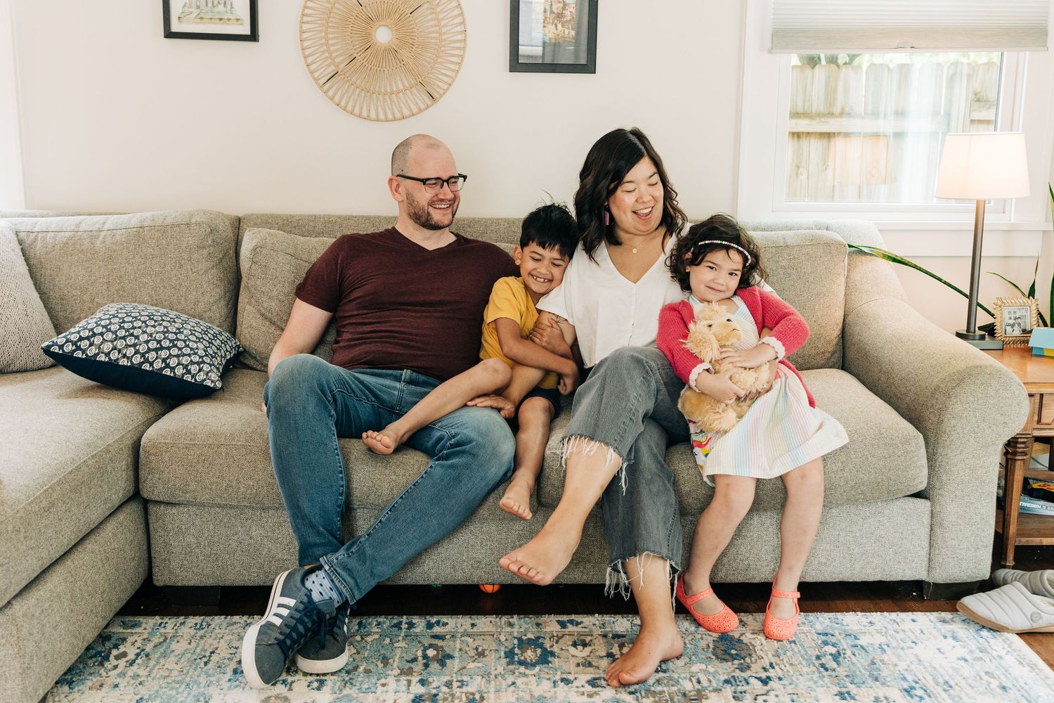 Four people relaxing together on a gray sectional sofa in a bright living room with area rug during Charlotte mini session.