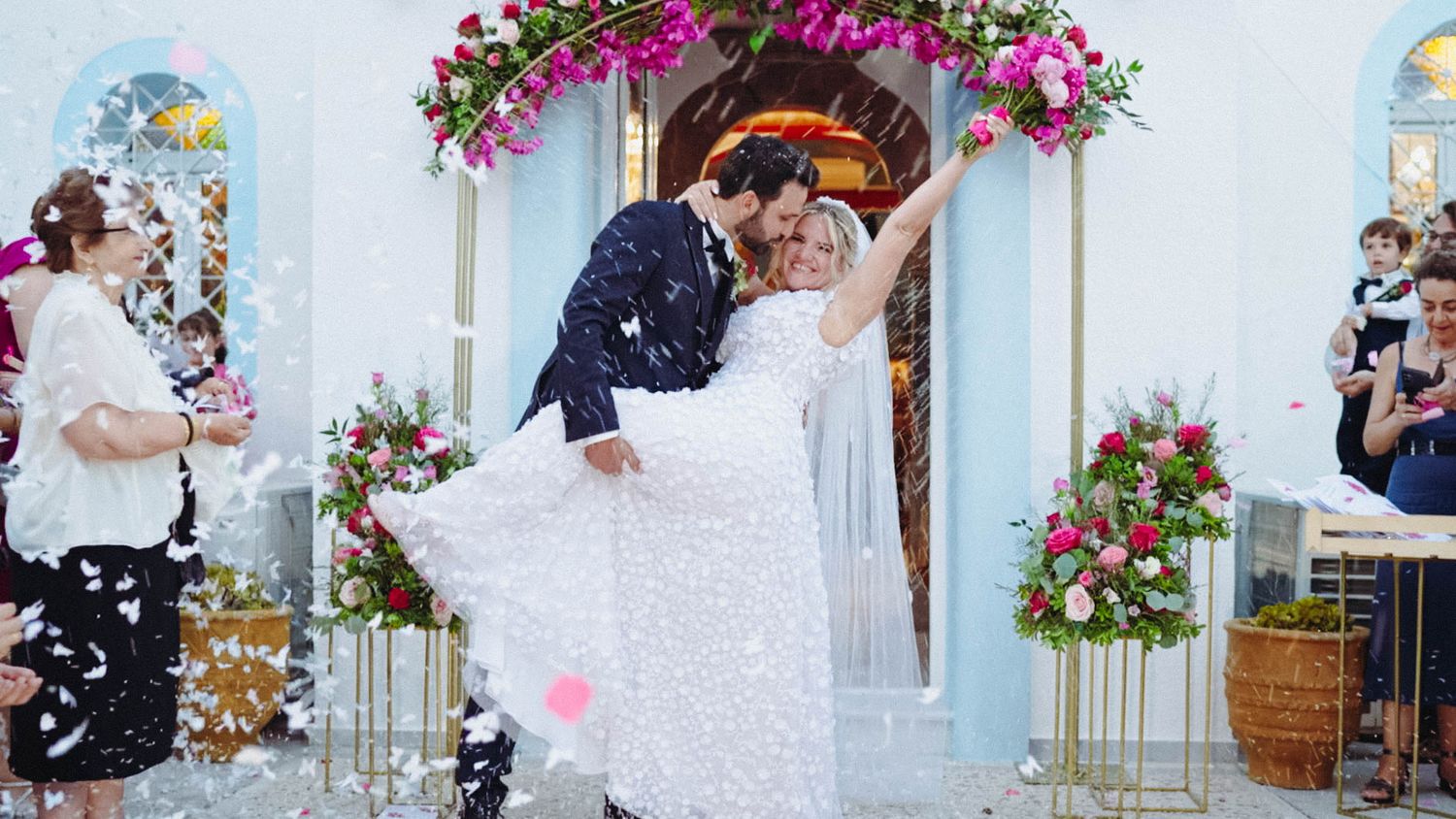 A joyous wedding ceremony under a floral arch with guests celebrating as confetti fills the winter air.