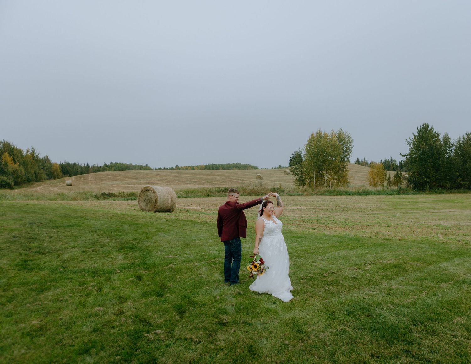 A couple shares a tender moment in a rural field with hay bales visible in the background.