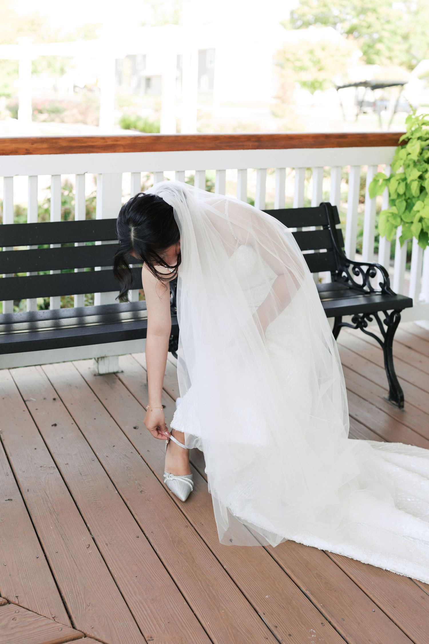 Wedding dress detail shot showing bride adjusting shoes on wooden porch.
