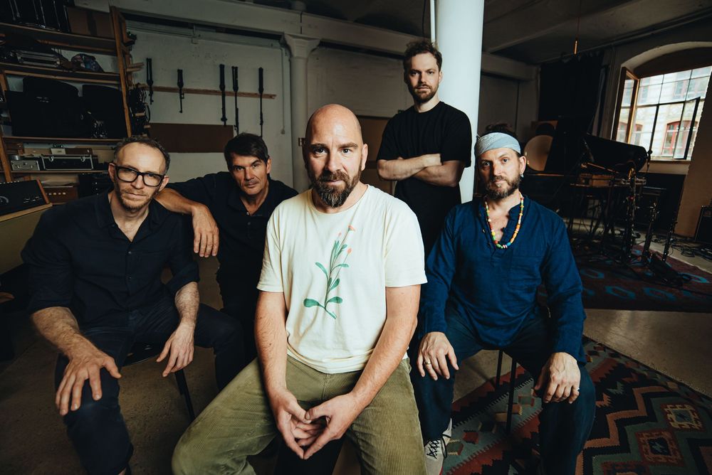 A group of five musicians pose together in a dimly lit room for a casual band photo.