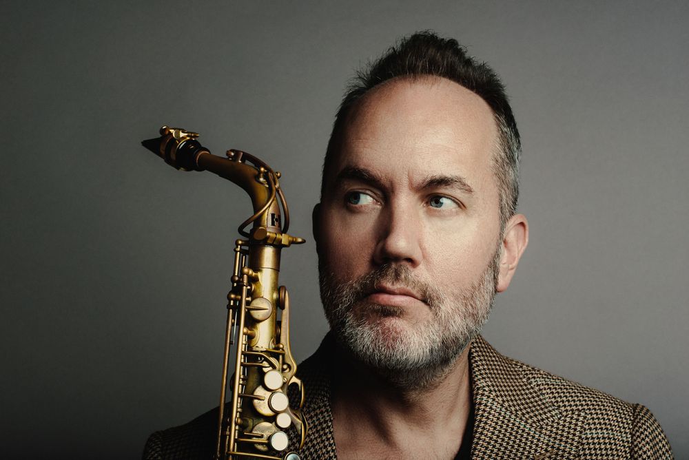 Close up studio portrait of a musician with a saxophone against a gray background in dramatic lighting.