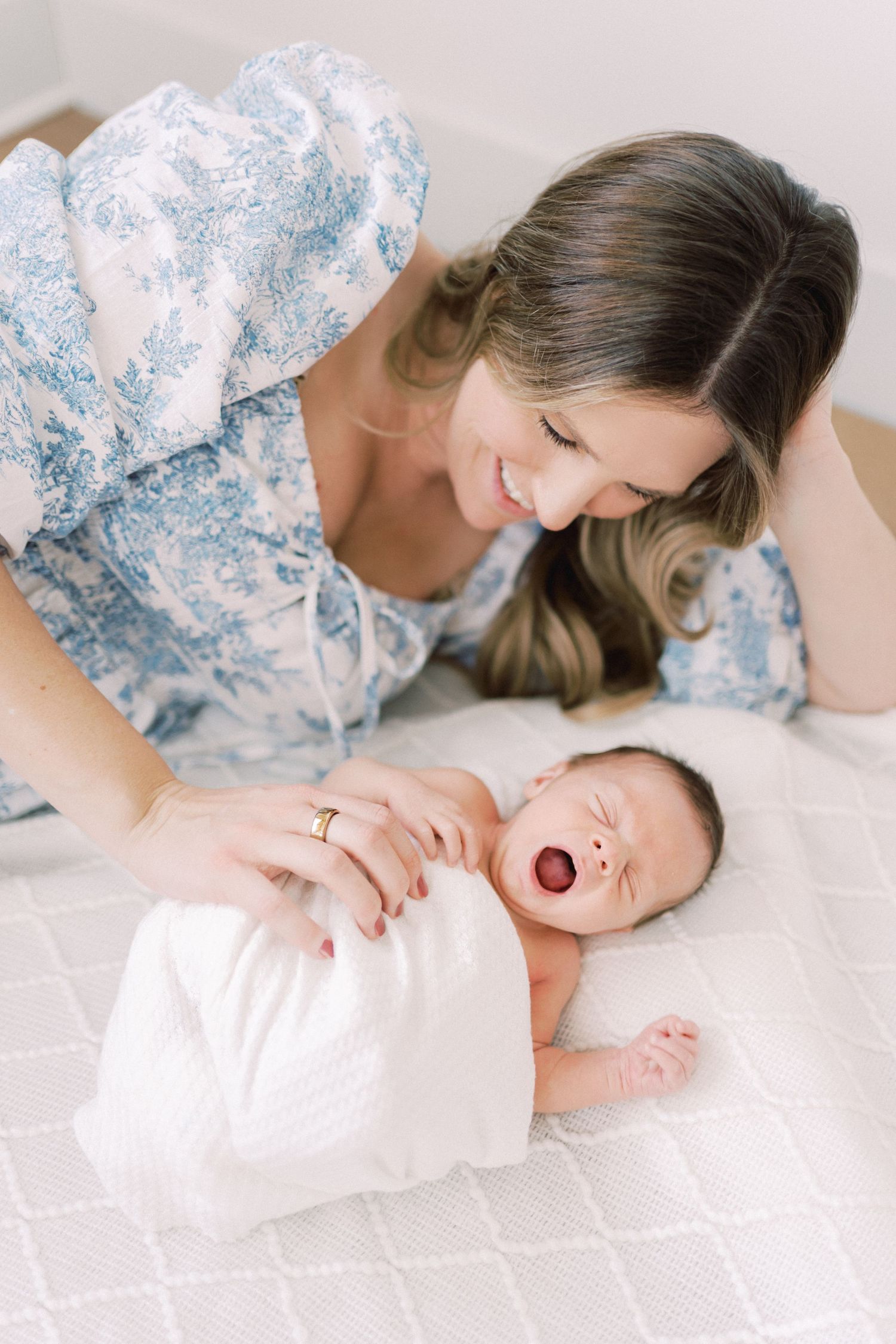 A tender moment captured between parent and yawning newborn baby on white bedding.