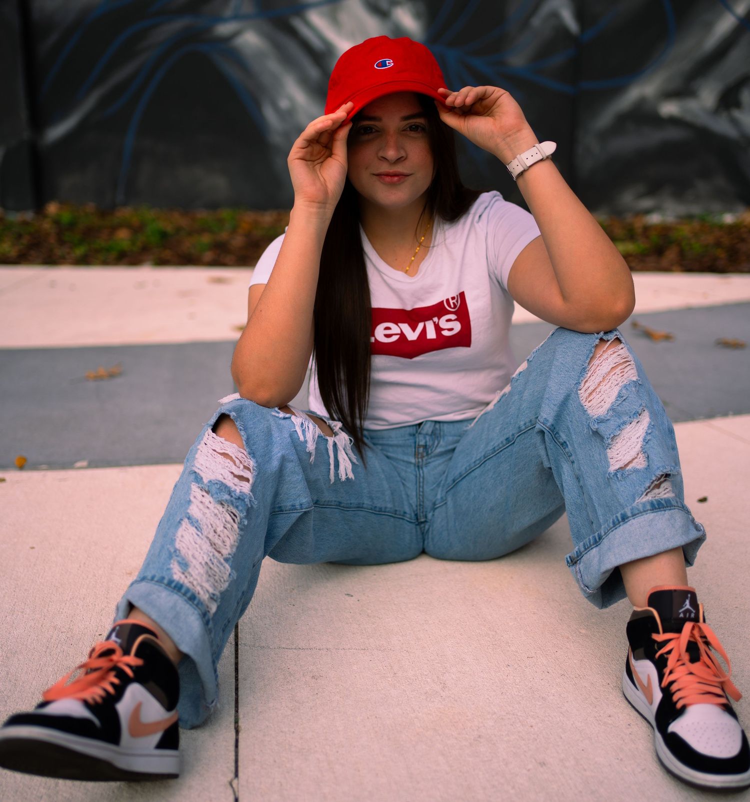 Casual street style photo of someone in ripped jeans and Levi's shirt sitting on pink concrete.