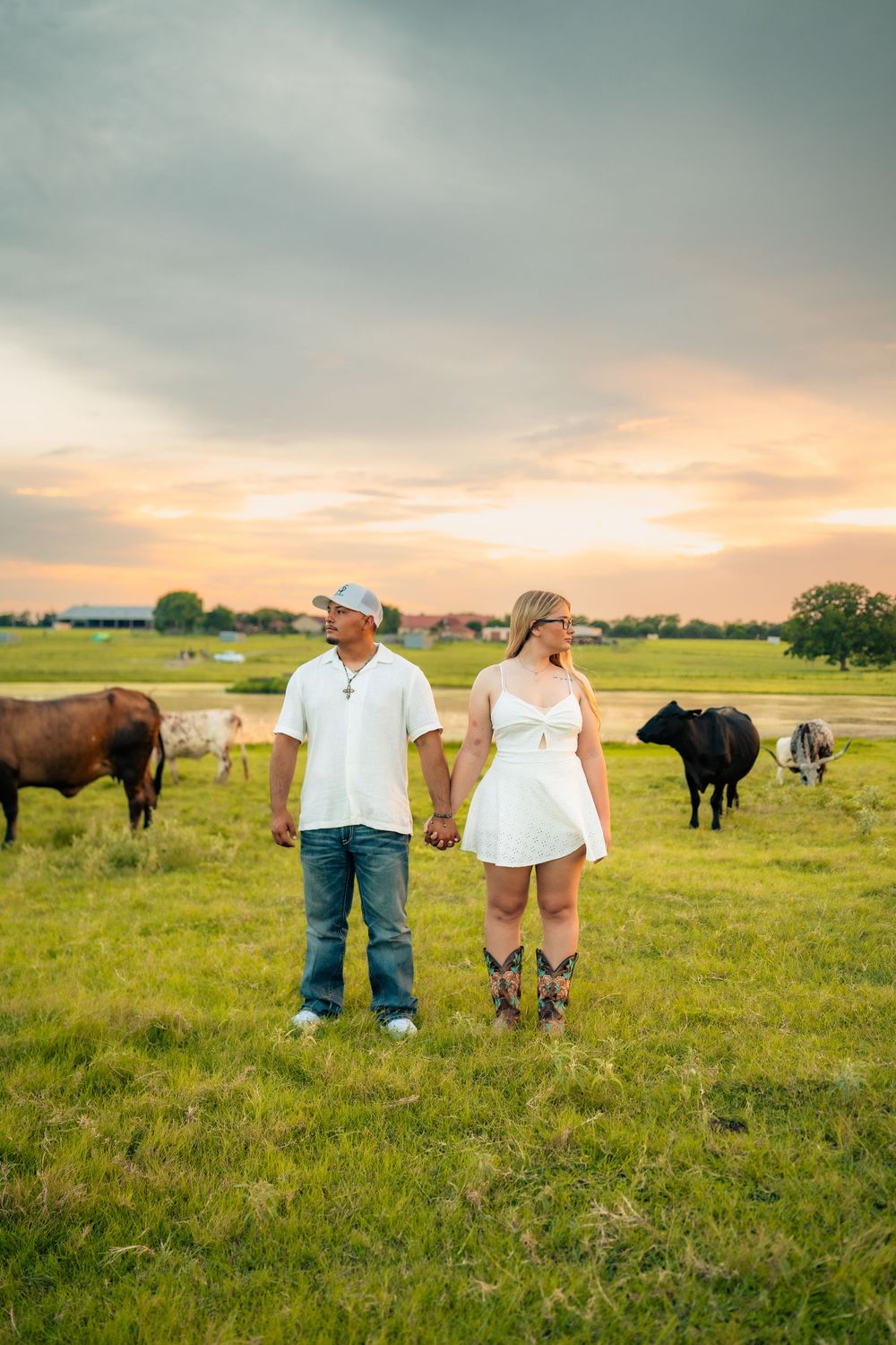 A couple enjoys a peaceful moment together in a rural pasture with grazing cattle and a sunset sky.
