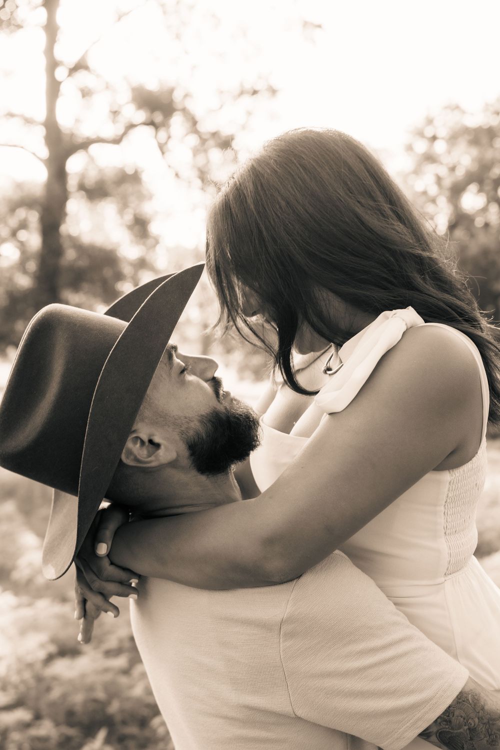 A romantic sepia-toned moment between two people embracing outdoors in soft natural lighting.