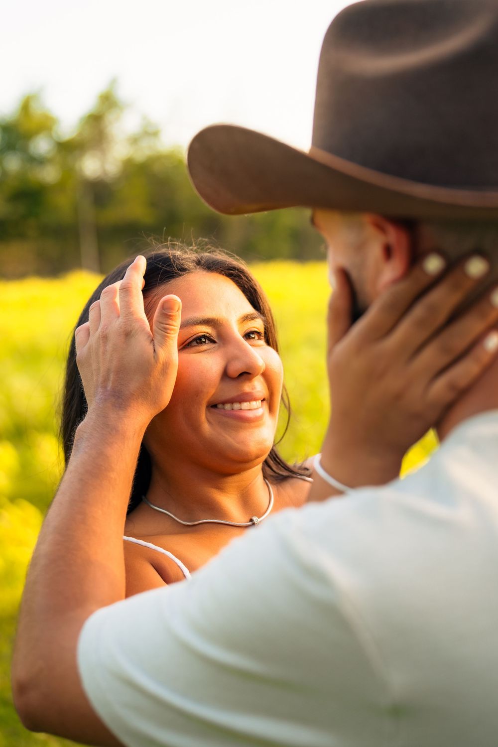 A couple shares a tender moment in golden sunlight, with one wearing a brown cowboy hat.