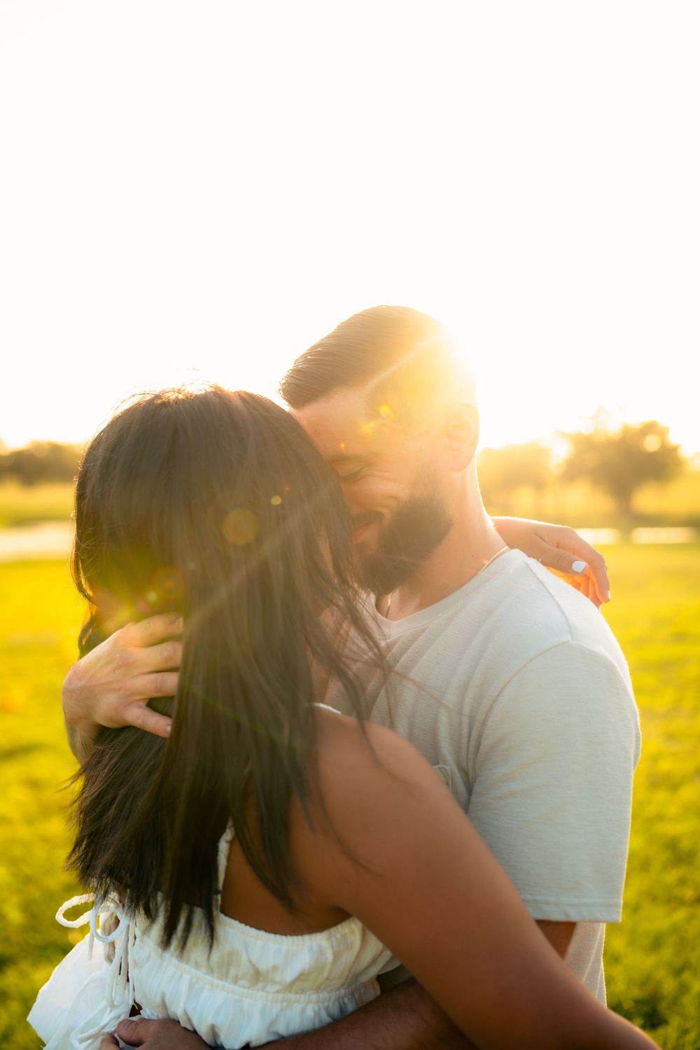Couple shares affectionate moment in golden sunlit field during sunset.