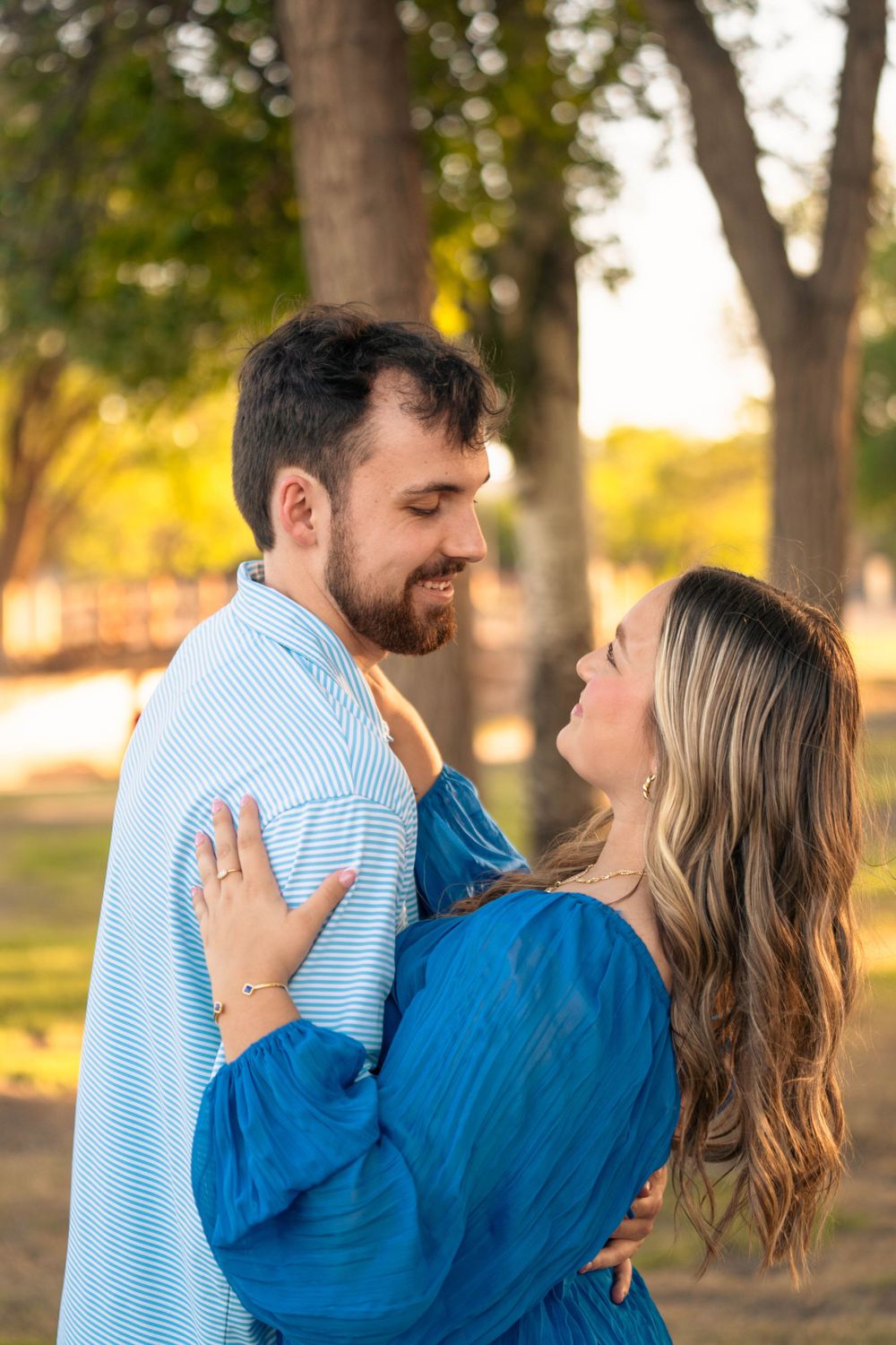 A romantic couple embraces outdoors in a park during golden hour.