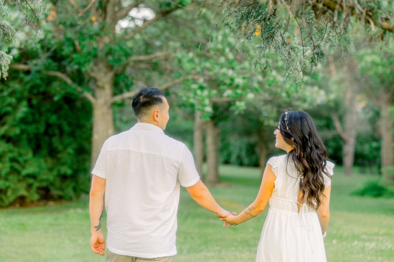 A couple holds hands while walking through a serene garden path on a sunny afternoon.